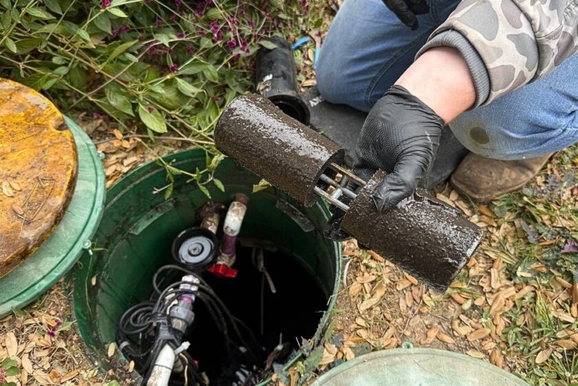 Technician holding the two halves of a clogged septic filter over the open pump tank riser