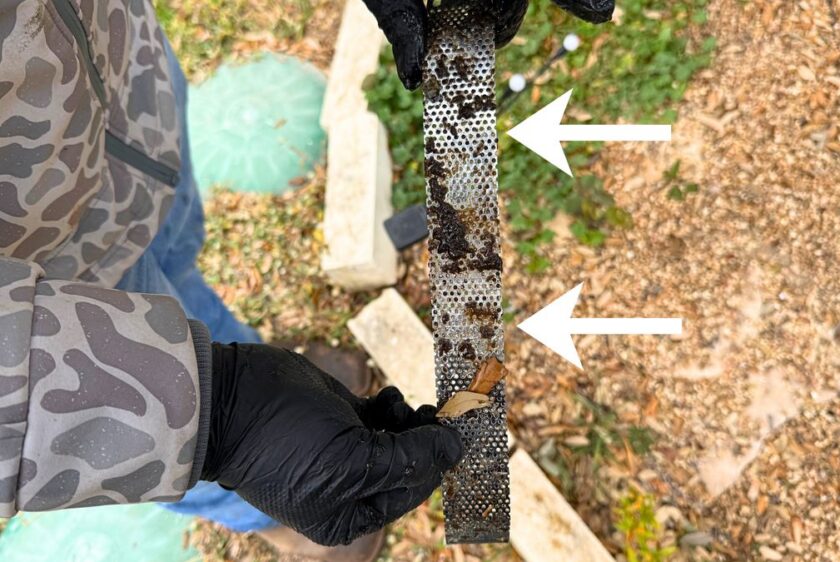 Mesh intake screen from a septic pump held up after removal, arrows pointing at the packed debris