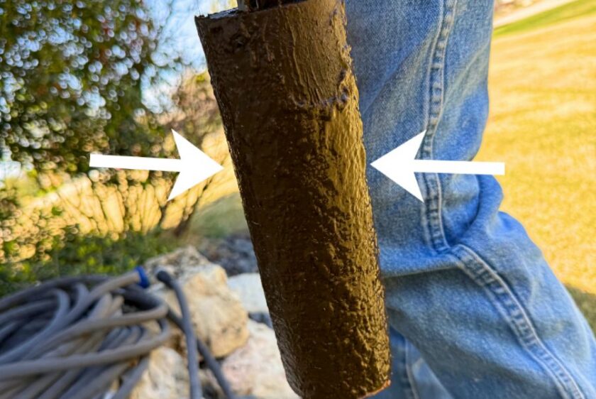 Septic filter pulled from the tank completely covered in sludge, arrows pointing at the clogged surface