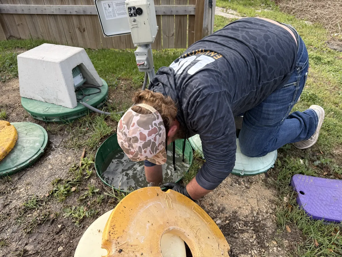Luna technician kneeling at an open aerobic septic tank lid during an inspection